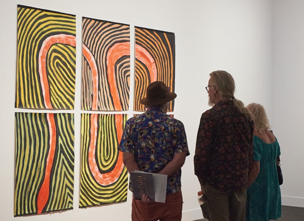 Three people looking at an indigenous artwork 